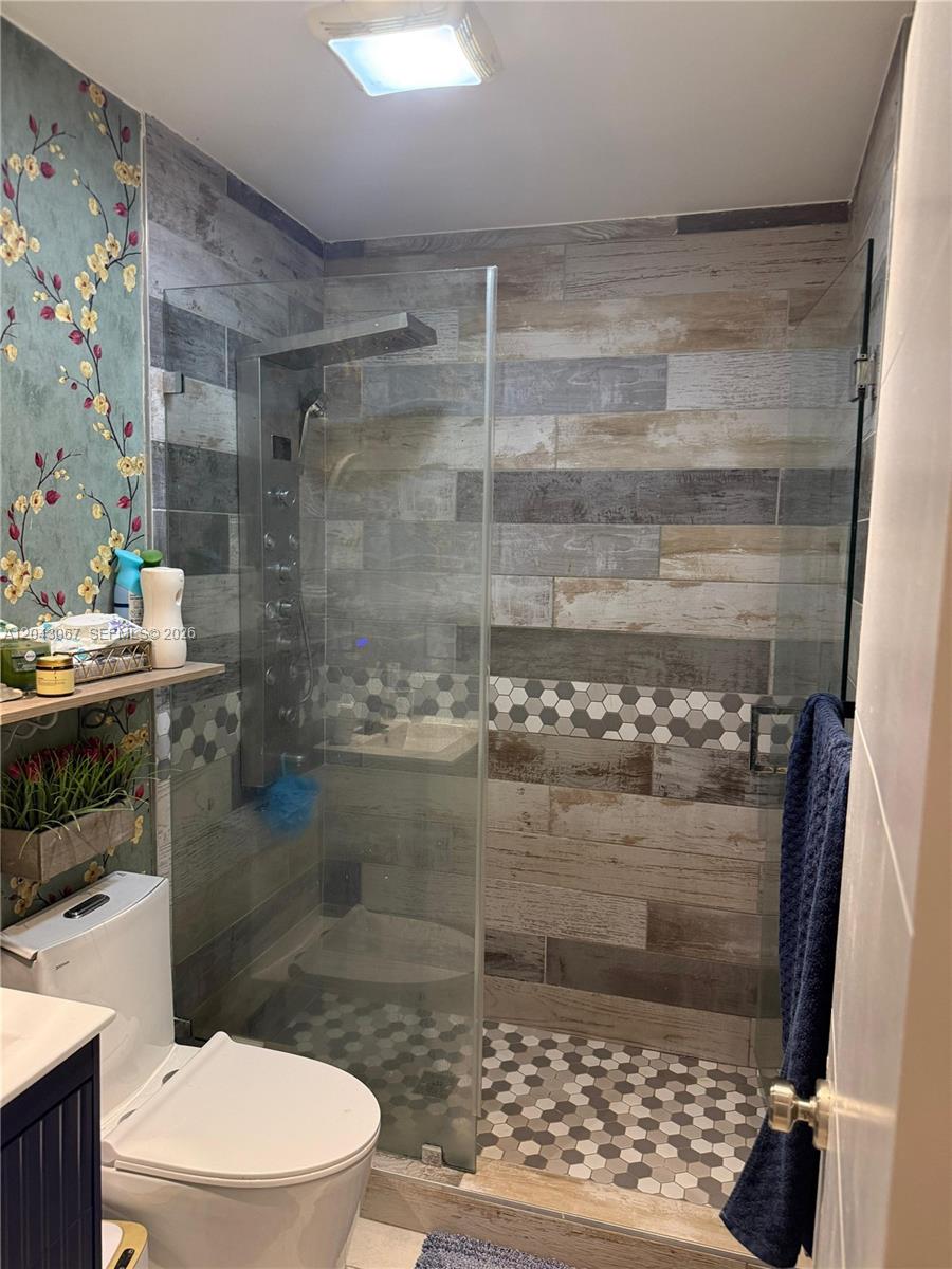 A bathroom features a glass-enclosed shower with wood-look tile, hexagonal floor tiles, and floral wallpaper — 6717 Simms St, Hollywood FL 33024, HOLLYWOOD, FL