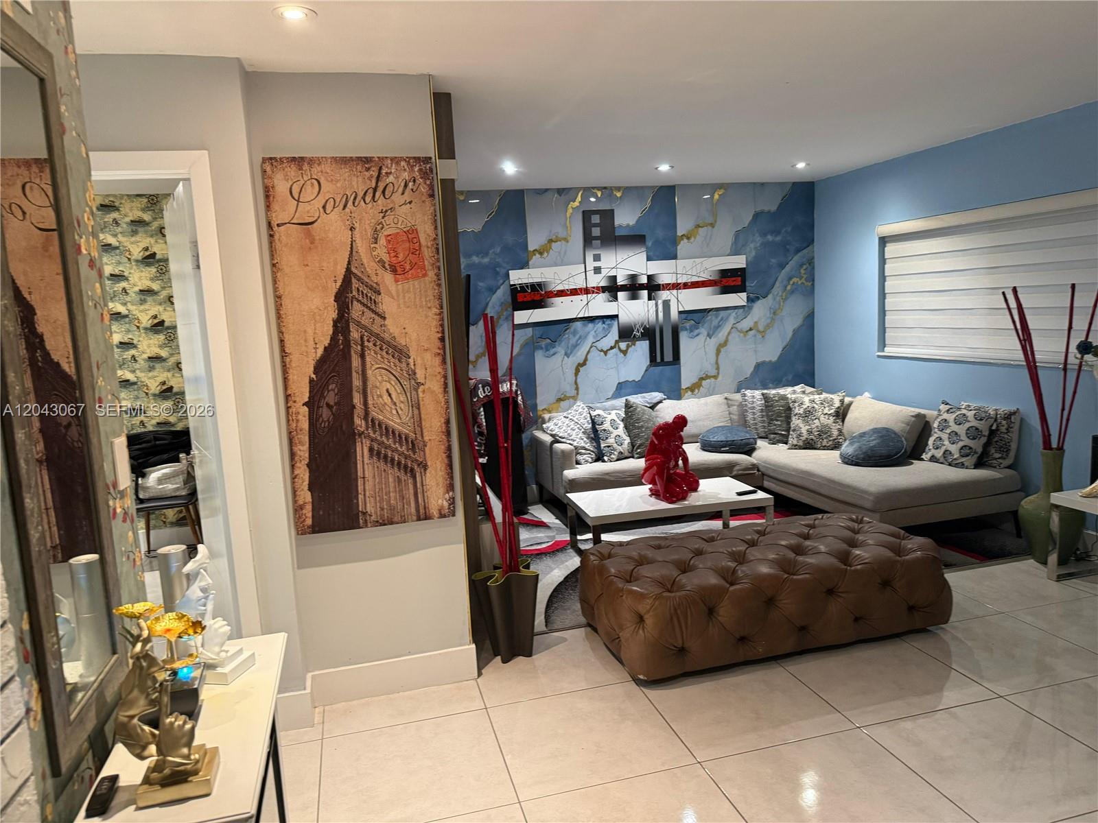 A living room features a sectional sofa, a tufted ottoman, and a large London-themed wall art — 6717 Simms St, Hollywood FL 33024, HOLLYWOOD, FL