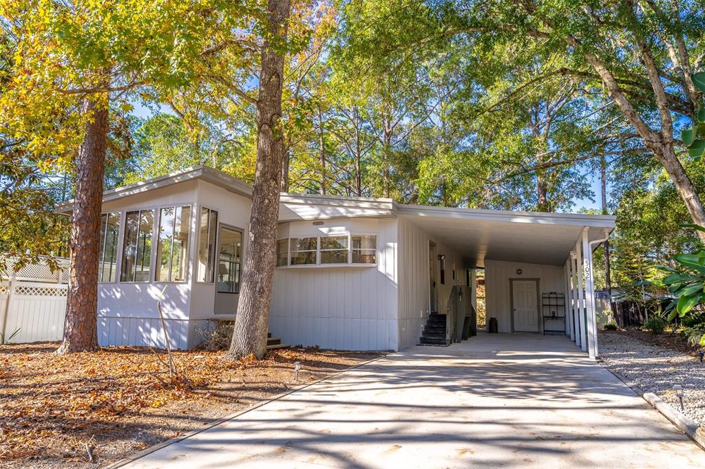 A light-colored mobile home with a carport and a sunroom sits among mature trees — 502 TIMBERLANE COURT, LAKE MARY, FL