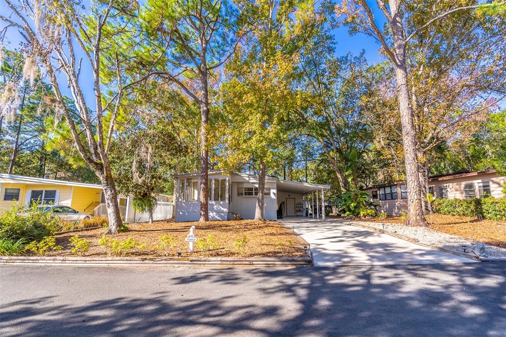 A single-story mobile home with a carport and a screened porch sits among tall trees — 502 TIMBERLANE COURT, LAKE MARY, FL