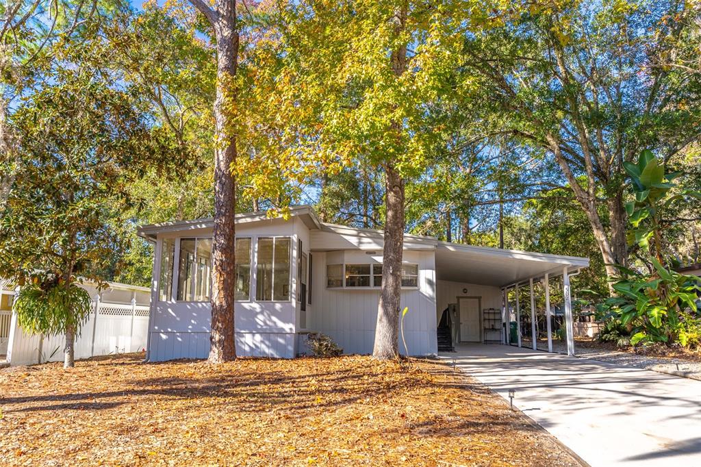 A light-colored mobile home features a screened-in porch, a carport, and surrounding mature trees — 502 TIMBERLANE COURT, LAKE MARY, FL