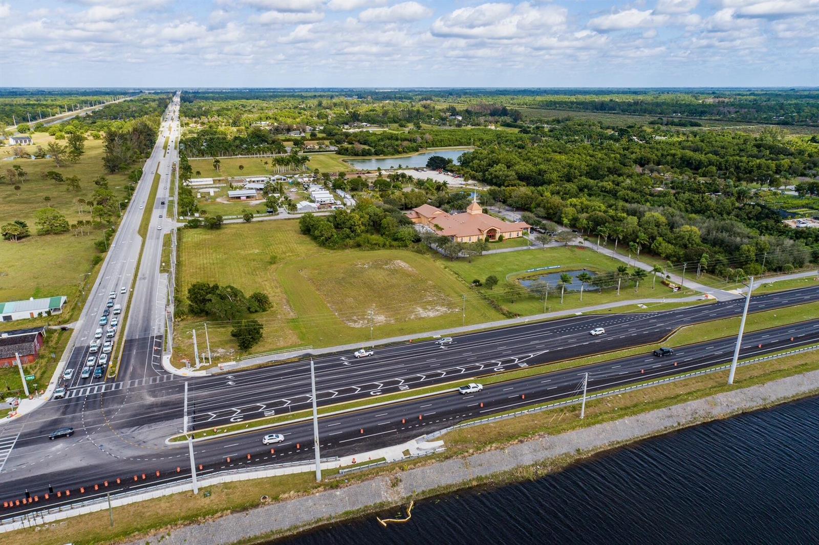 An aerial view shows a large building with a steeple near a highway and canal — 16670 Rembrandt Road, Wellington FL, WELLINGTON, FL