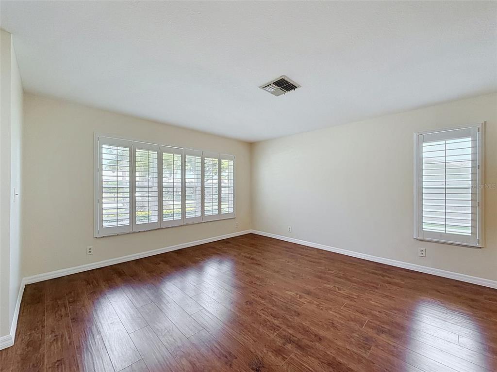 An empty room features wood-look flooring, beige walls, and white plantation shutters on the windows — 3068 E DORCHESTER DRIVE, PALM HARBOR, FL