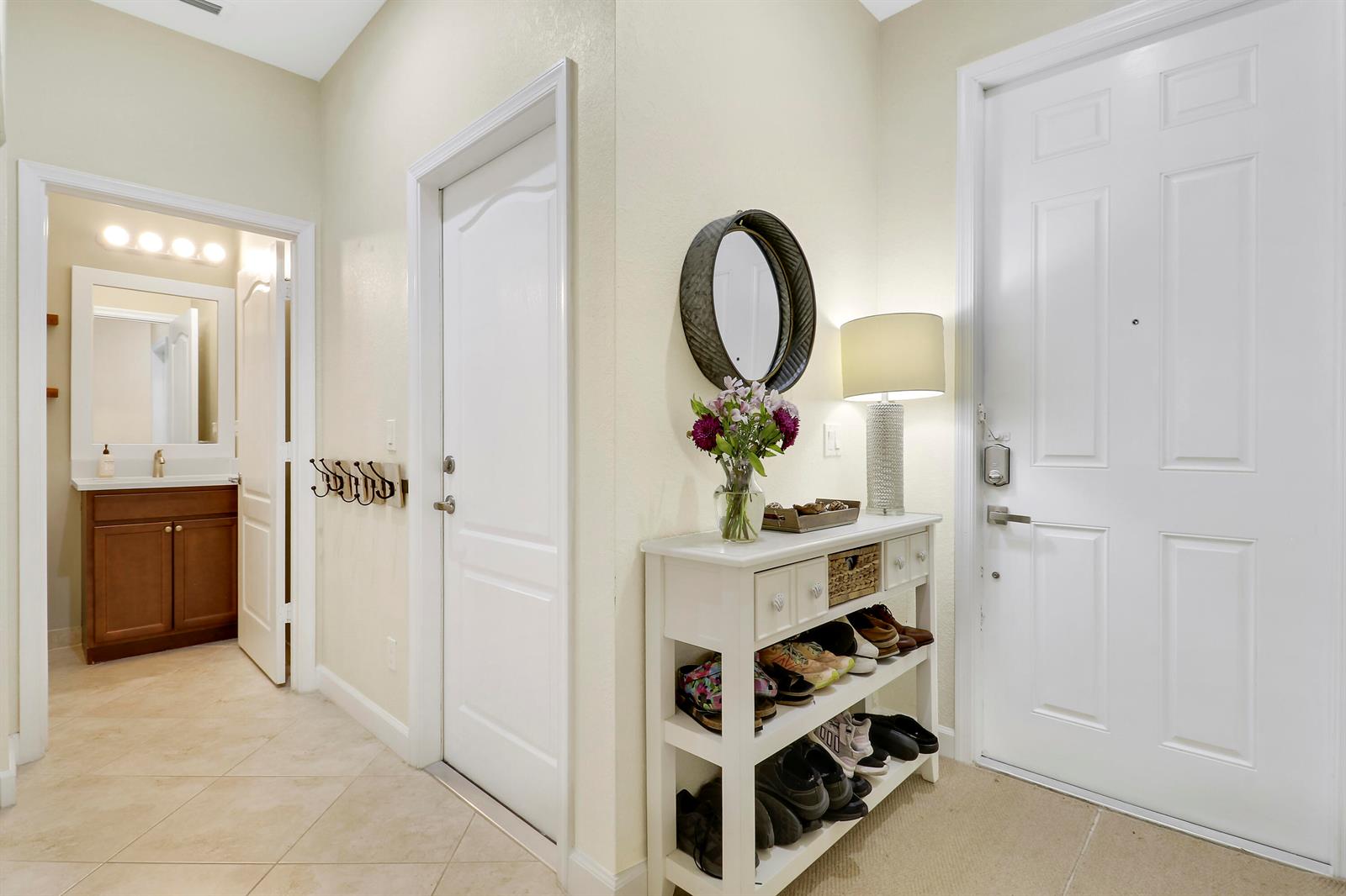 An entryway features a white console table with shoe storage, a mirror, and a nearby bathroom — 9504 SW Merlin Court, Stuart FL 34997, STUART, FL
