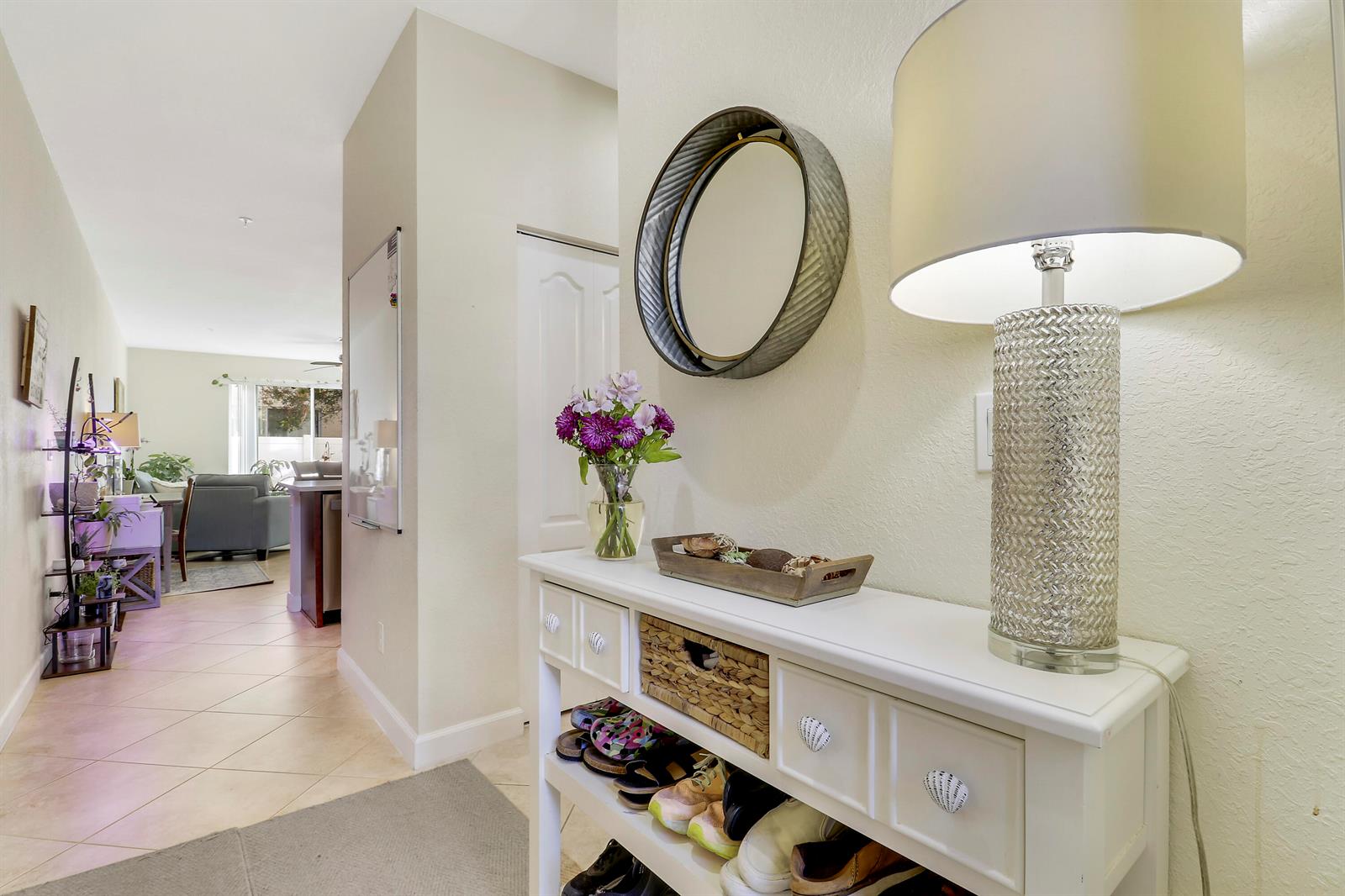 A white entryway console table with a lamp and mirror sits in a tiled hallway — 9504 SW Merlin Court, Stuart FL 34997, STUART, FL