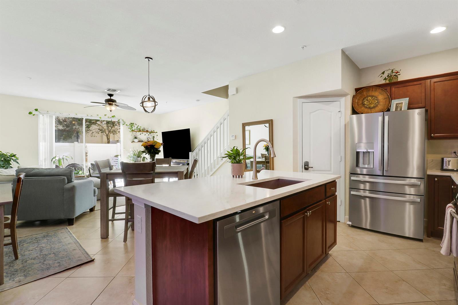 A kitchen island with a stainless steel dishwasher faces a living area and dining space — 9504 SW Merlin Court, Stuart FL 34997, STUART, FL