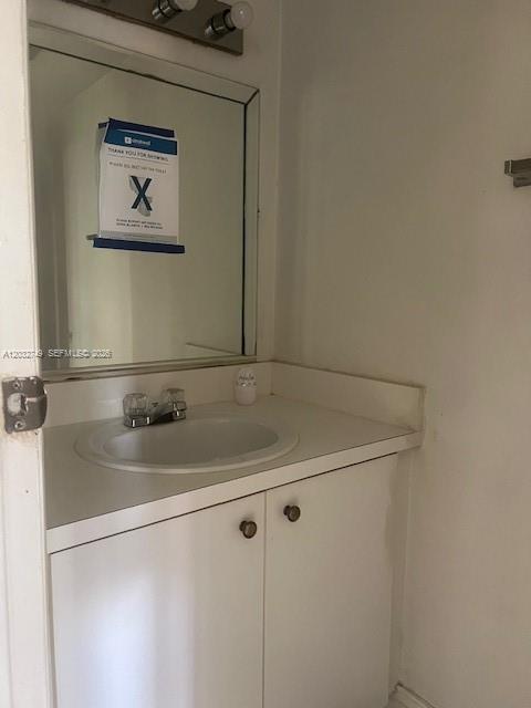 A bathroom vanity with a white cabinet, a sink, and a mirror with a sign — 17911 NW 68th Ave # P208, Hialeah FL 33015, HIALEAH, FL
