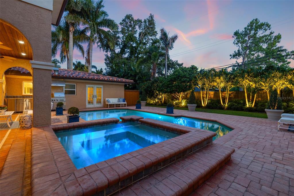 A backyard patio features a swimming pool, a raised hot tub, and palm trees at dusk — 1124 SEVILLE LANE NE, ST PETERSBURG, FL