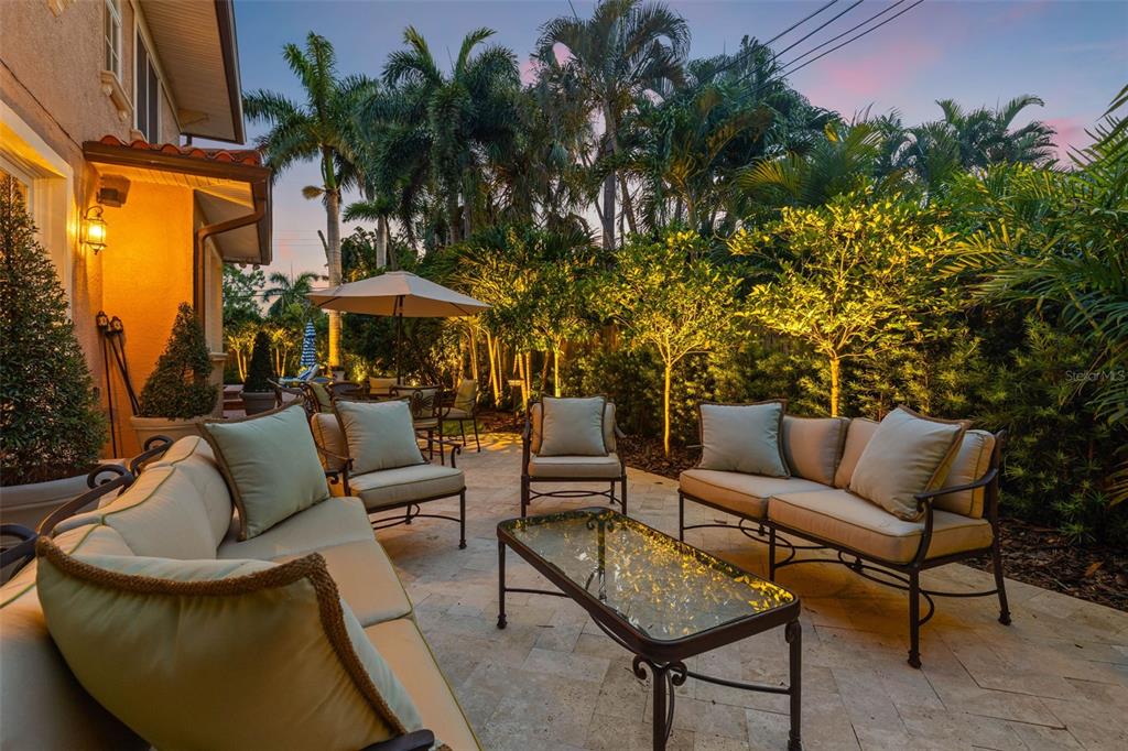 A furnished outdoor patio features a stone floor, seating area, and lush tropical landscaping — 1124 SEVILLE LANE NE, ST PETERSBURG, FL