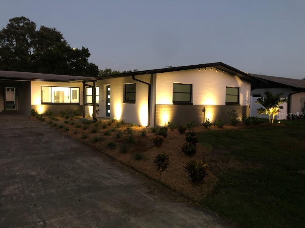 A single-story house with a white and gray exterior, illuminated by modern landscape lighting — 909 MARABON AVENUE, ORLANDO, FL