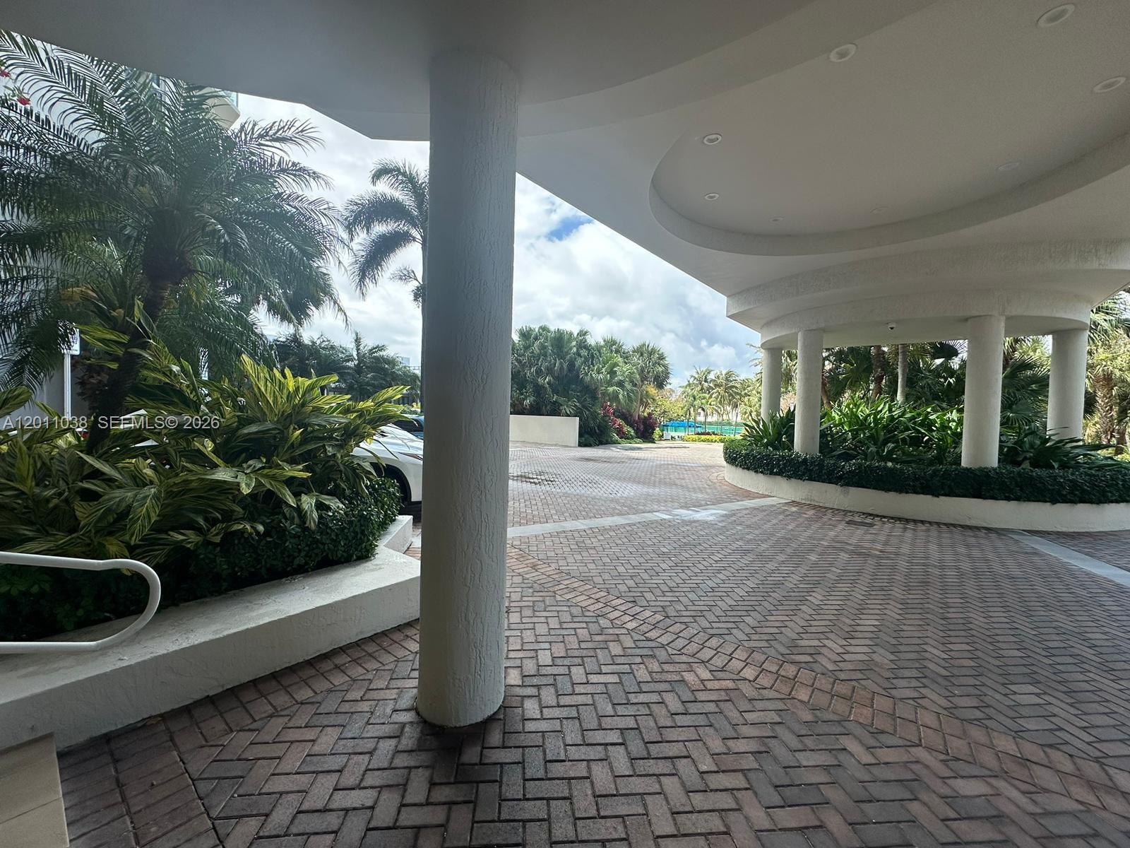 A paved driveway leads under a covered porte-cochère supported by white columns near tropical landscaping — 6001 N Ocean Dr # 503, Hollywood FL 33019, HOLLYWOOD, FL