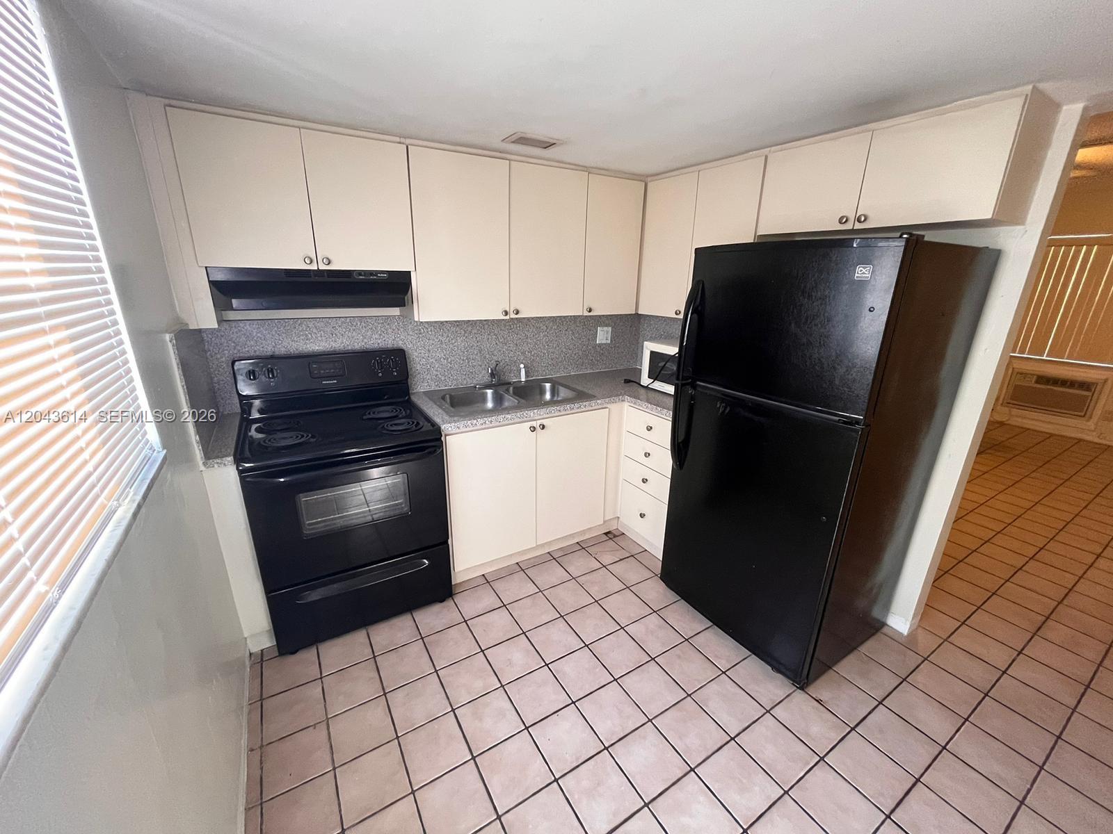 A small kitchen features off-white cabinets, black appliances, a double sink, and tiled flooring — 13 NE 2nd Ave # 104, Dania Beach FL 33004, DANIA BEACH, FL