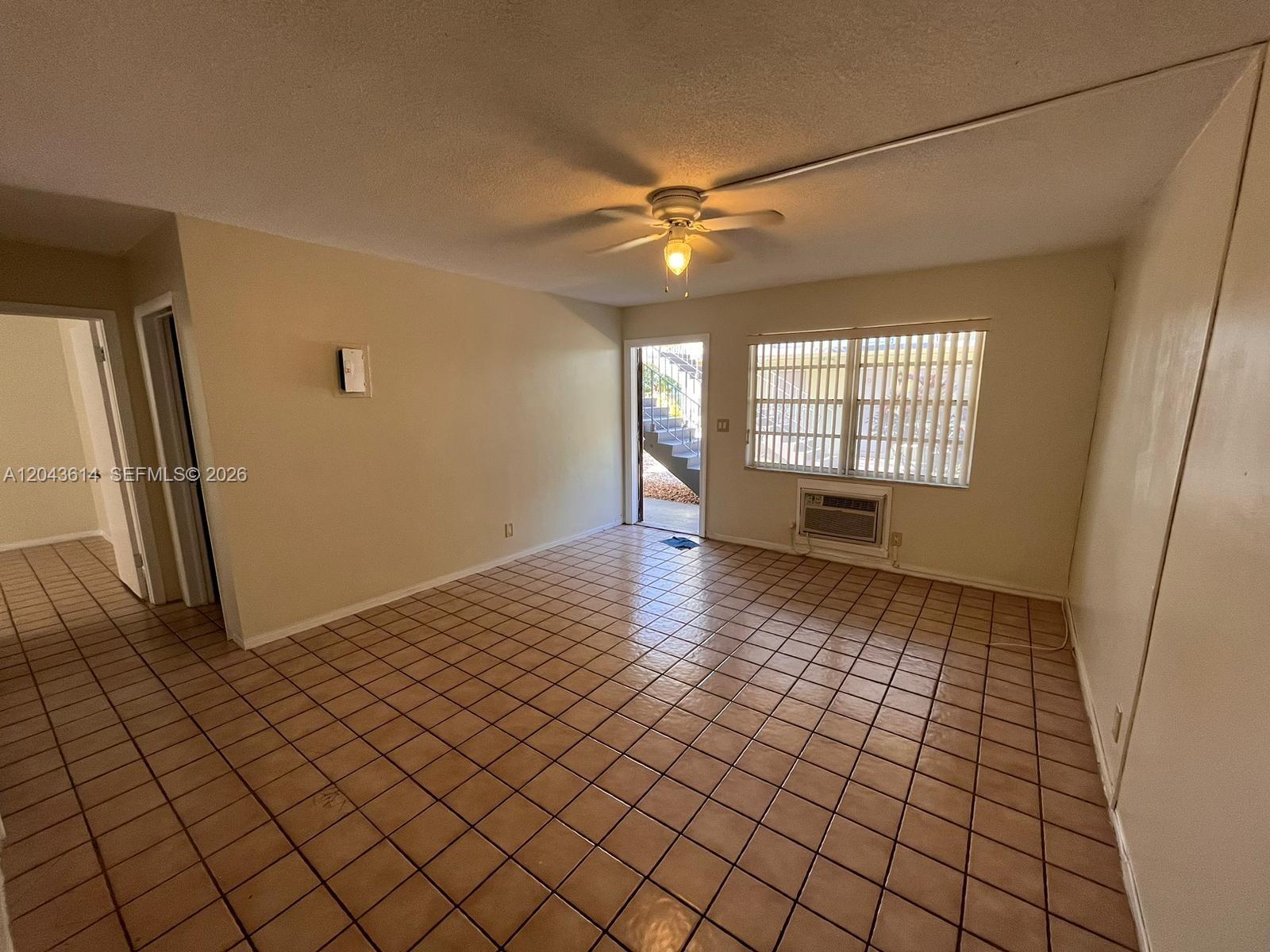 An empty room features beige tile flooring, a ceiling fan, and a window air conditioner — 13 NE 2nd Ave # 104, Dania Beach FL 33004, DANIA BEACH, FL