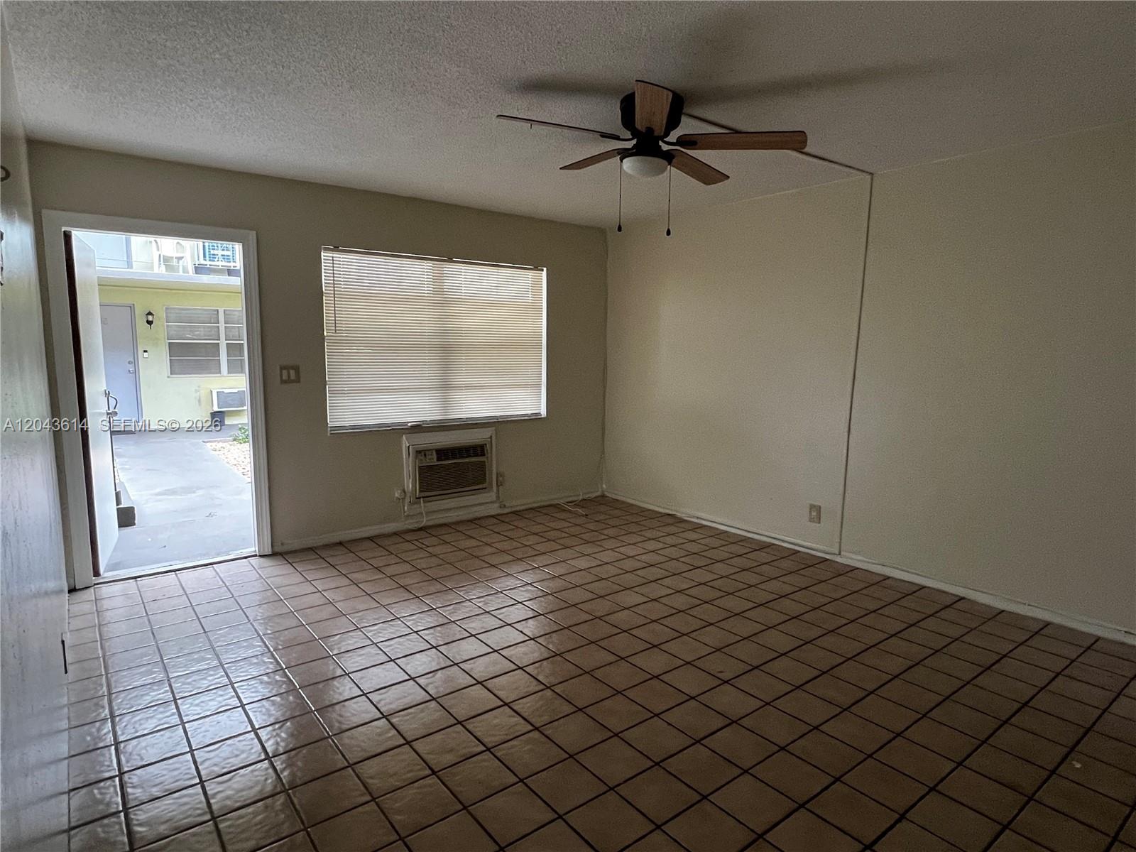 An empty room features tan tile flooring, a ceiling fan, and an open exterior door — 13 NE 2nd Ave # 104, Dania Beach FL 33004, DANIA BEACH, FL