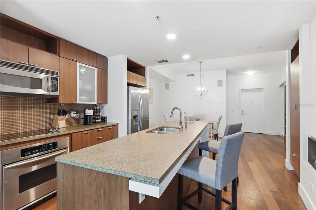 A kitchen features wood cabinetry, stainless steel appliances, a stone island, and bar seating — 111 N 12TH STREET UNIT 1325, TAMPA, FL