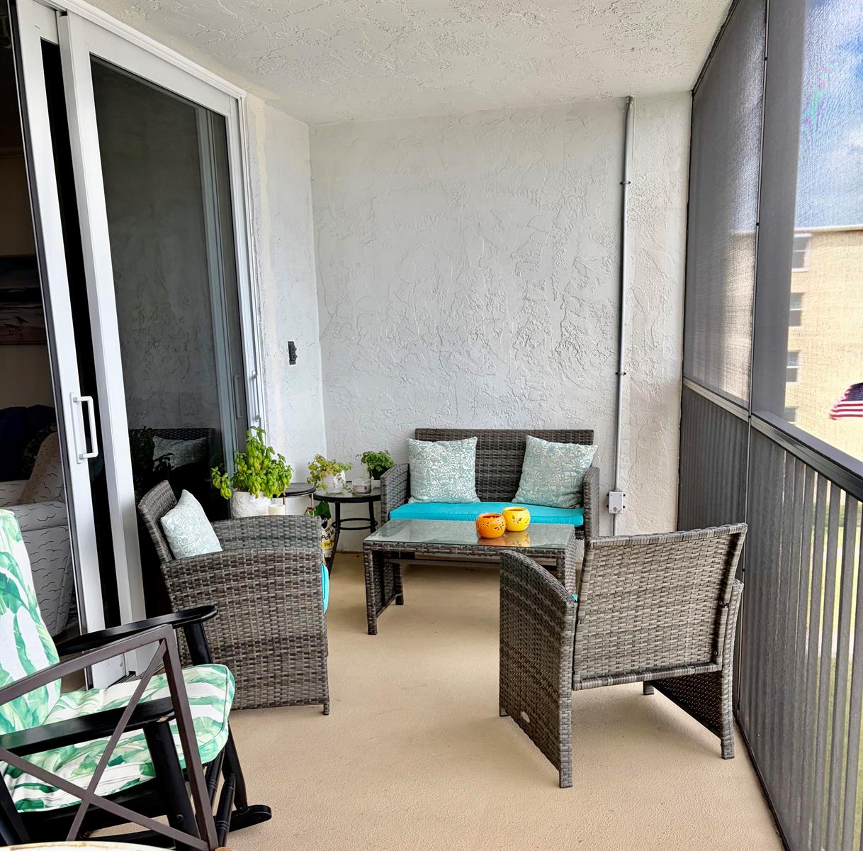 A screened-in balcony features wicker patio furniture, a glass-top coffee table, and sliding glass doors — 740 E Ocean Avenue # 407, Boynton Beach FL 33435, BOYNTON BEACH, FL