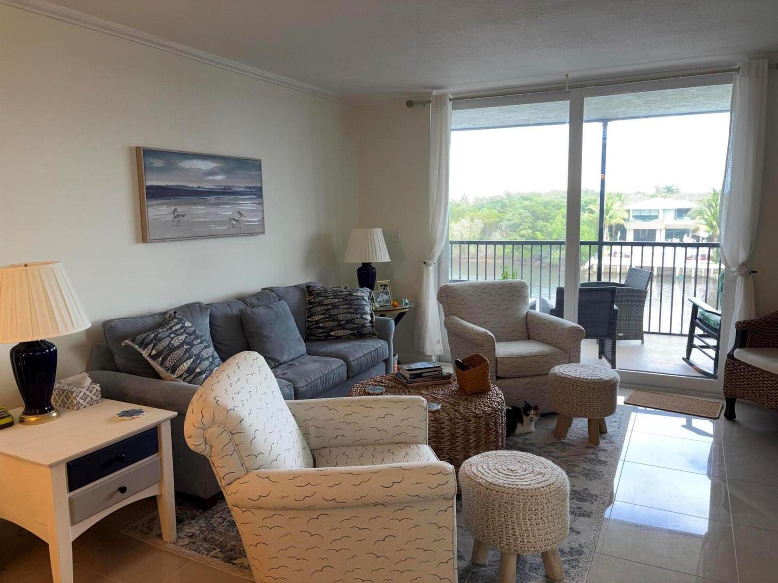 A living room with a grey sofa, patterned armchairs, and a balcony overlooking the water — 740 E Ocean Avenue # 407, Boynton Beach FL 33435, BOYNTON BEACH, FL