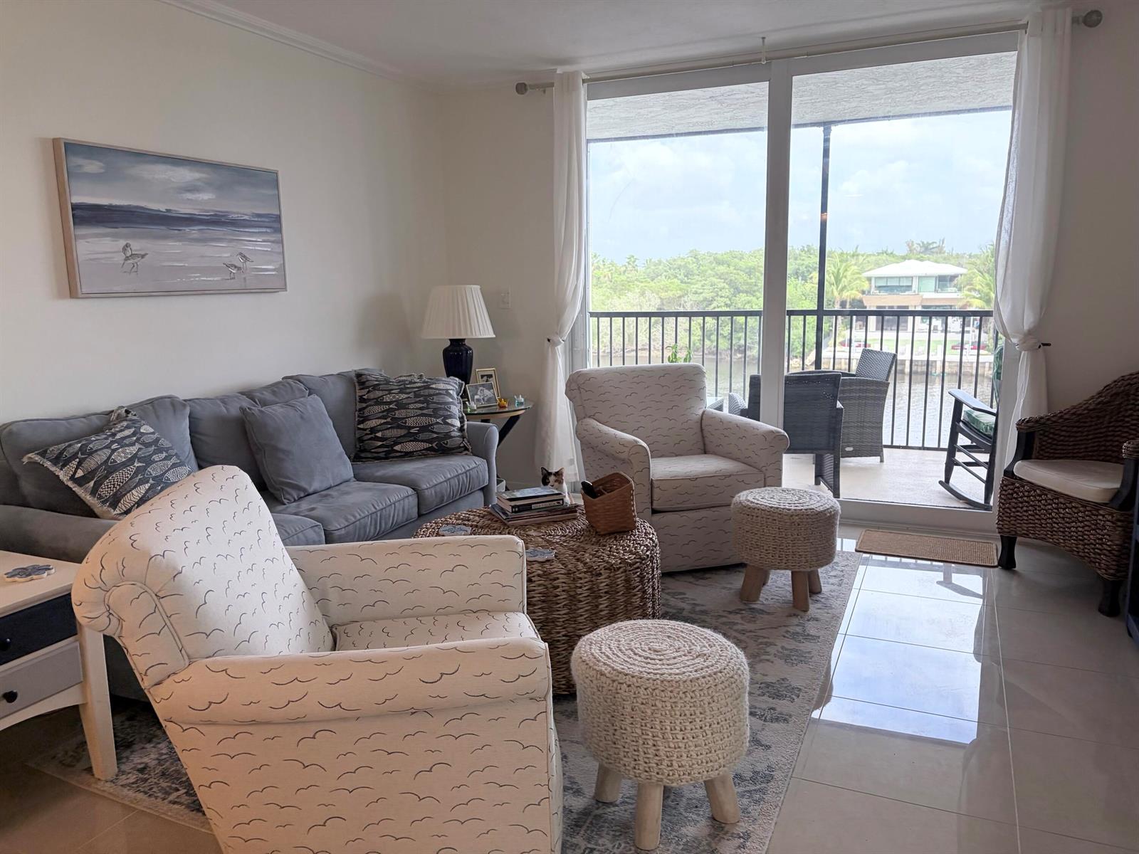 A living room features a gray sofa, patterned armchairs, a woven coffee table, and balcony access — 740 E Ocean Avenue # 407, Boynton Beach FL 33435, BOYNTON BEACH, FL