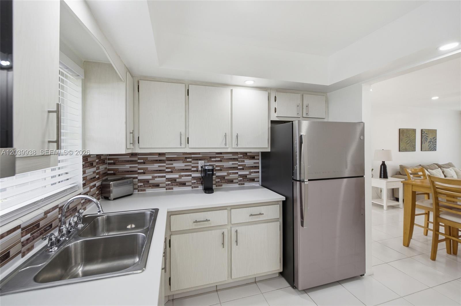 A kitchen features white cabinets, stainless steel appliances, a double sink, and a tiled backsplash — 2894 E Crosley Dr E # D, West Palm Beach FL 33415, WEST PALM BEACH, FL
