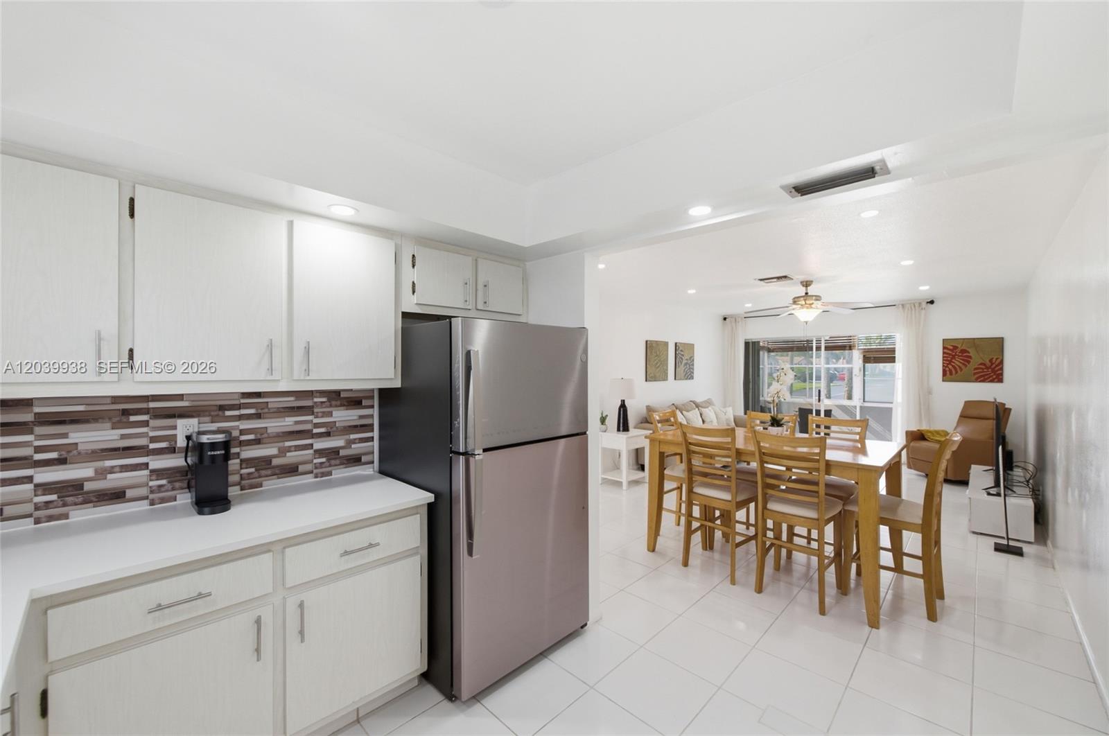 A kitchen with white cabinets and a stainless steel refrigerator opens to a dining area — 2894 E Crosley Dr E # D, West Palm Beach FL 33415, WEST PALM BEACH, FL