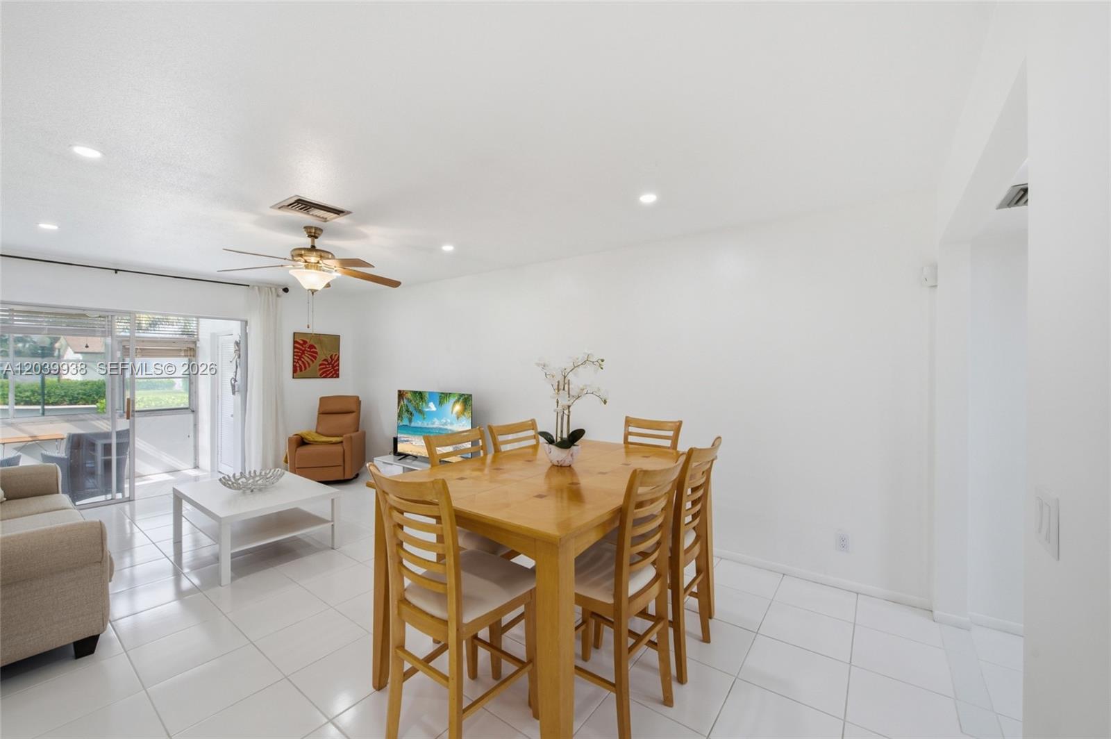 A dining area and living room with white tile floors, a wooden table, and sliding doors — 2894 E Crosley Dr E # D, West Palm Beach FL 33415, WEST PALM BEACH, FL