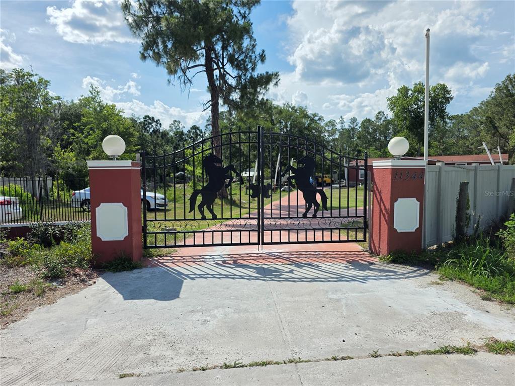 A black metal gate with horse silhouettes stands between two red stucco pillars — 11344 ROCKRIDGE ROAD, LAKELAND, FL
