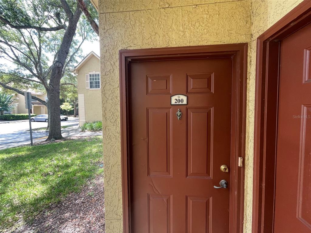 A brown exterior door with the number 200 is set into a textured yellow wall — 850 GRAND REGENCY POINT UNIT 200, ALTAMONTE SPRINGS, FL
