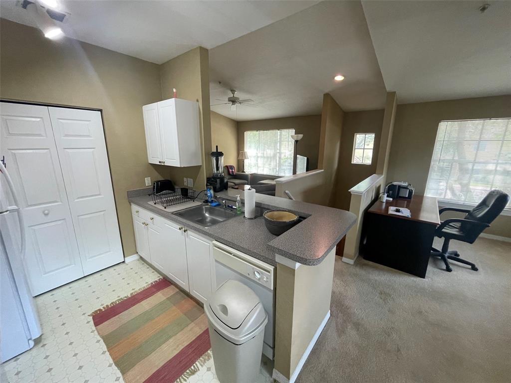 A kitchen with white cabinets and a breakfast bar overlooks a carpeted office area — 850 GRAND REGENCY POINT UNIT 200, ALTAMONTE SPRINGS, FL