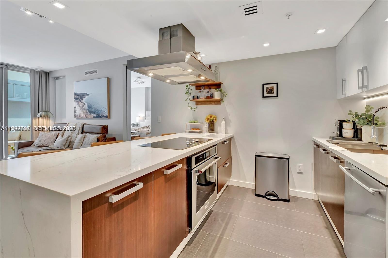 A modern kitchen features wood-toned cabinetry, white marble countertops, and a stainless steel range hood — 720 NE 62nd St # 307, Miami FL 33138, MIAMI, FL
