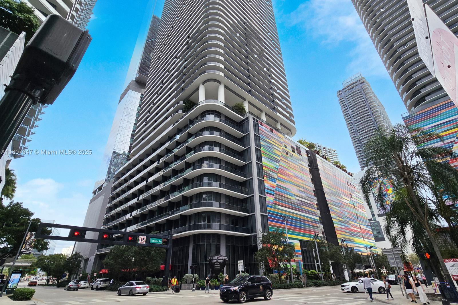 A low-angle exterior view of a modern high-rise building featuring a colorful striped facade — 801 S Miami Ave # 2201, Miami FL 33130, MIAMI, FL