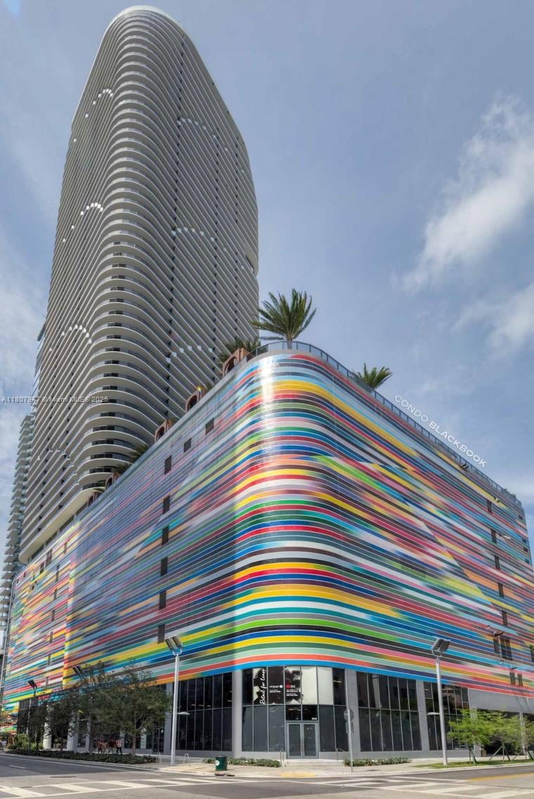 A tall, modern residential tower rises above a multi-story parking garage with a colorful striped facade — 801 S Miami Ave # 2201, Miami FL 33130, MIAMI, FL