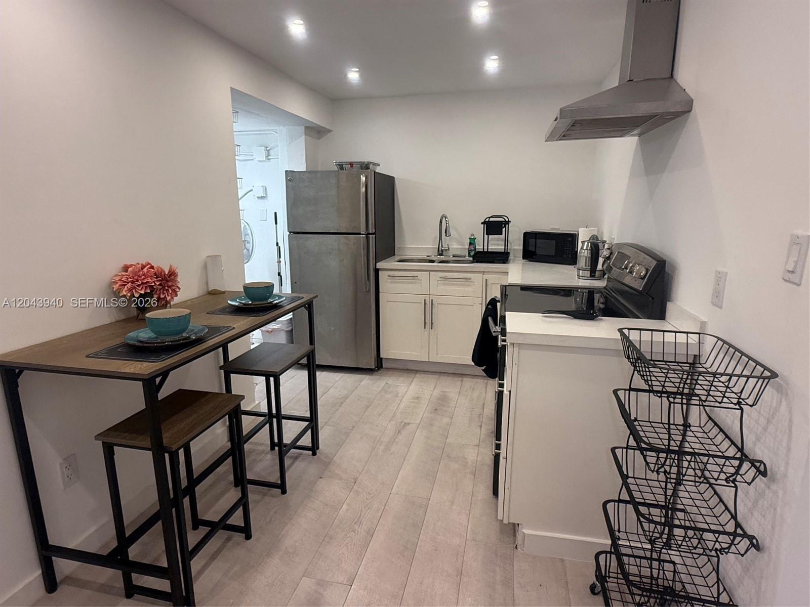 A small kitchen features white cabinets, stainless steel appliances, and a wooden dining table — 1947 Garfield St # 2, Hollywood FL 33020, HOLLYWOOD, FL