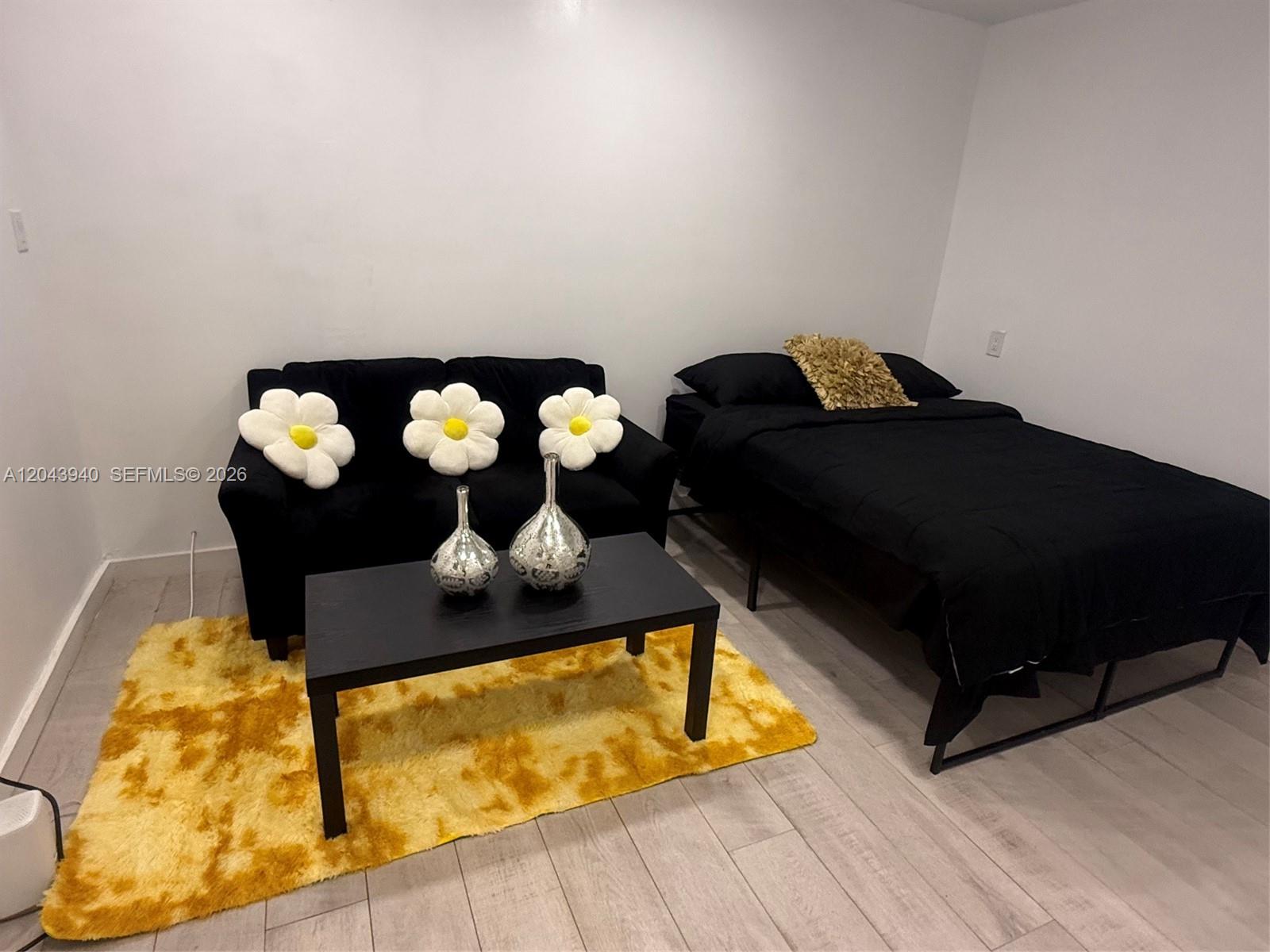 A bedroom features a black sofa with flower pillows, a coffee table, and a bed — 1947 Garfield St # 2, Hollywood FL 33020, HOLLYWOOD, FL