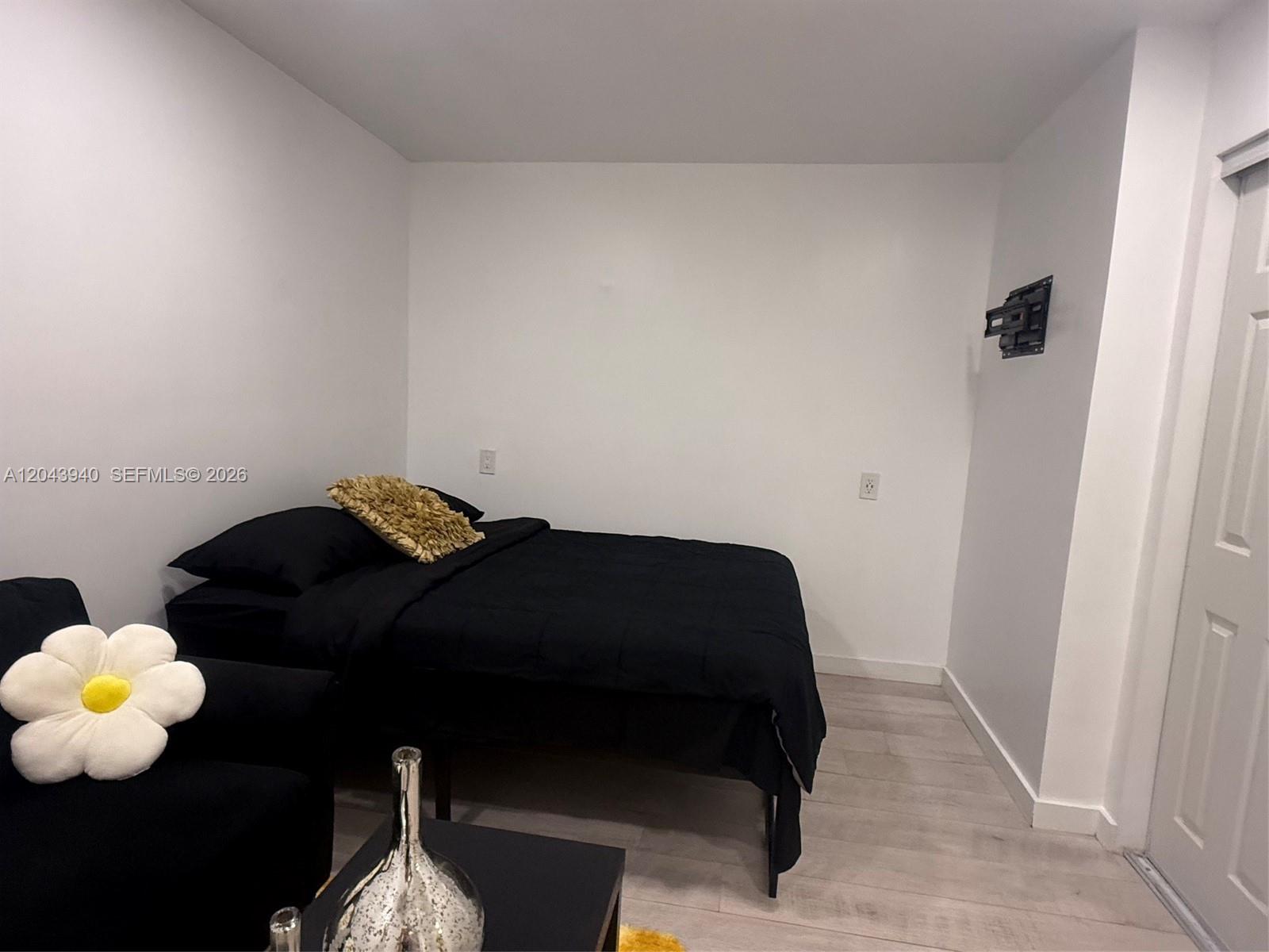 A bedroom features a black bed, light wood-look flooring, and a wall-mounted television bracket — 1947 Garfield St # 2, Hollywood FL 33020, HOLLYWOOD, FL