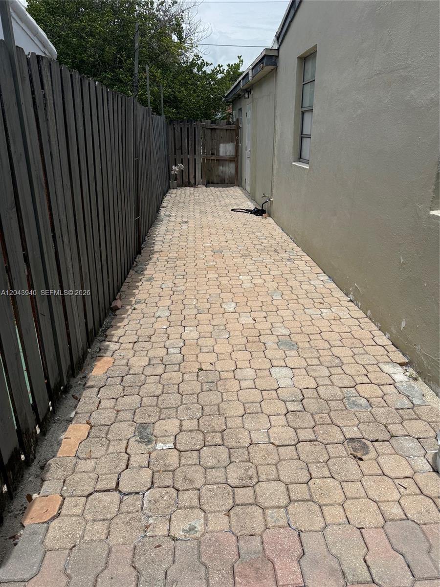A narrow outdoor walkway features light-colored interlocking pavers between a wooden fence and a building — 1947 Garfield St # 2, Hollywood FL 33020, HOLLYWOOD, FL