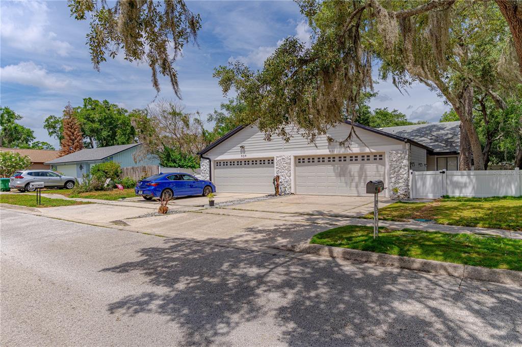 A single-story duplex with two garage doors, light-colored siding, and stone accents under large trees — 911 ROBINHOOD COURT, MAITLAND, FL