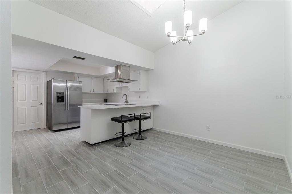 A kitchen with white cabinets, stainless steel appliances, a breakfast bar, and gray tile flooring — 911 ROBINHOOD COURT, MAITLAND, FL