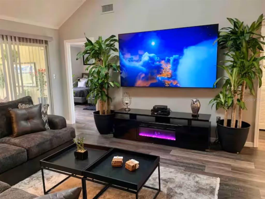 A living room features a large wall-mounted television, an electric fireplace console, and two plants — 1160 VILLA LANE UNIT 108, APOPKA, FL