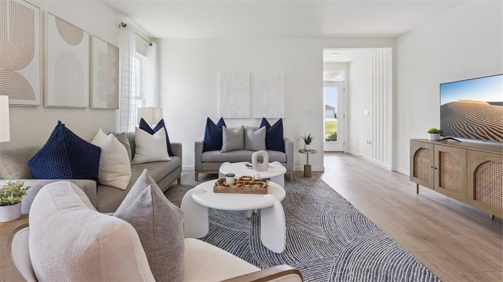 A living room features light wood flooring, gray sofas, white coffee tables, and a television — 4910 MARSHELDER STREET, APOPKA, FL