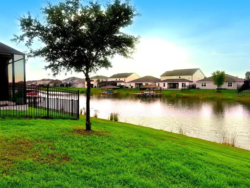 A grassy backyard overlooks a pond with boat docks and houses in the distance — 5055 TIBET COURT, ST CLOUD, FL