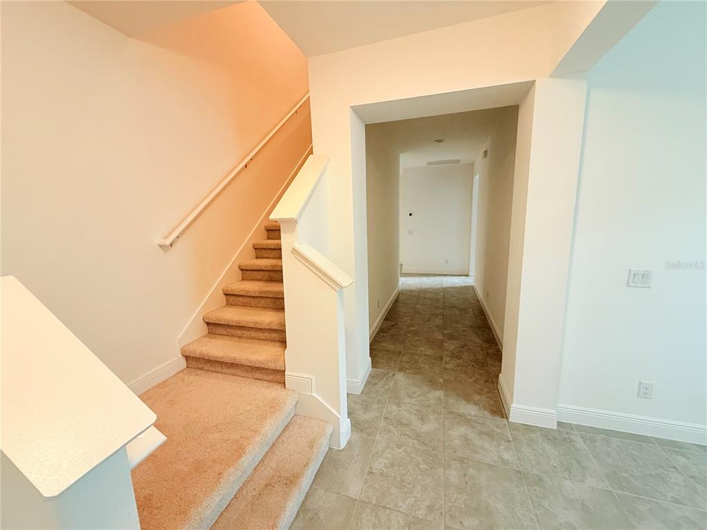 A carpeted staircase leads upward next to a tiled hallway in a bright interior space — 5055 TIBET COURT, ST CLOUD, FL