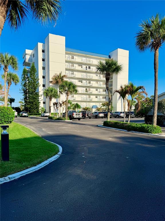 A multi-story white apartment building stands behind a paved parking lot with palm trees — 5151 N HIGHWAY A1A UNIT 212, HUTCHINSON ISLAND, FL