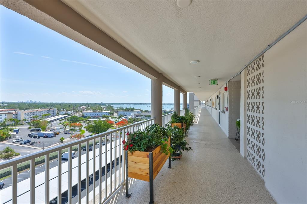 An outdoor balcony walkway features a metal railing, wooden planters, and a view of water — 5980 SHORE BOULEVARD S UNIT 907, GULFPORT, FL