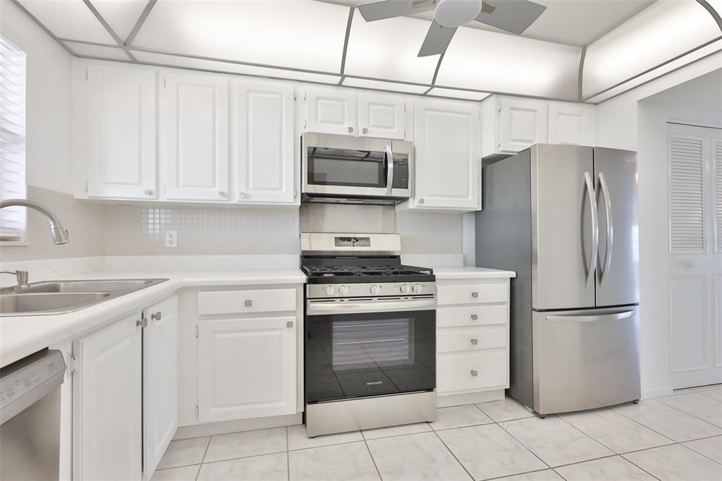 A kitchen with white cabinets, stainless steel appliances, and light-colored tile flooring — 5980 SHORE BOULEVARD S UNIT 907, GULFPORT, FL