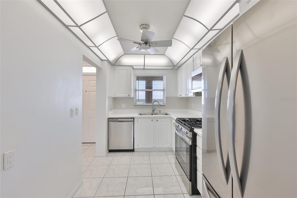 A bright kitchen features white cabinets, stainless steel appliances, tile flooring, and a ceiling fan — 5980 SHORE BOULEVARD S UNIT 907, GULFPORT, FL