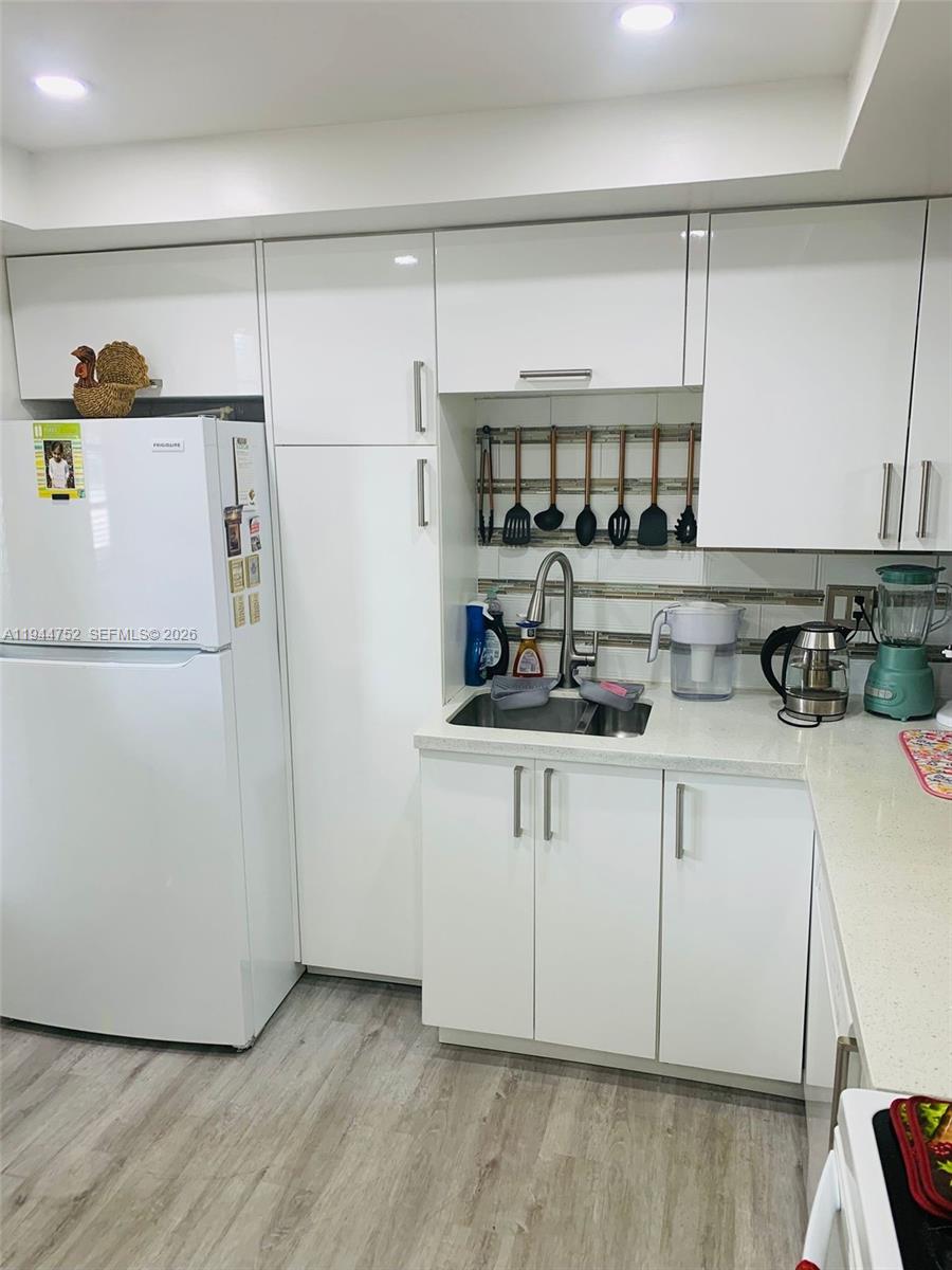 A kitchen features white cabinetry, a white refrigerator, a stainless steel sink, and light flooring — 1333 E Hallandale Beach Blvd # 131, Hallandale Beach FL 33009, HALLANDALE BEACH, FL