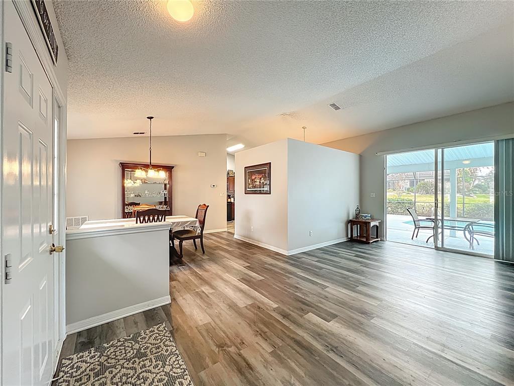 A living and dining area with wood-look flooring, a half wall, and sliding glass doors — 3850 PLANTATION BOULEVARD, LEESBURG, FL