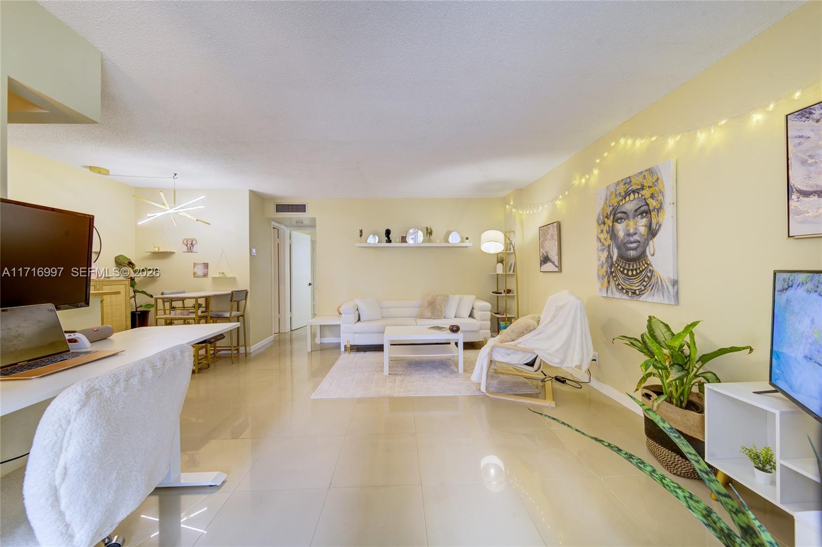 A bright living room features light-colored tile floors, a white sofa, and decorative wall art — 1040 SE 4th Ave # 128, Deerfield Beach FL 33441, DEERFIELD BEACH, FL
