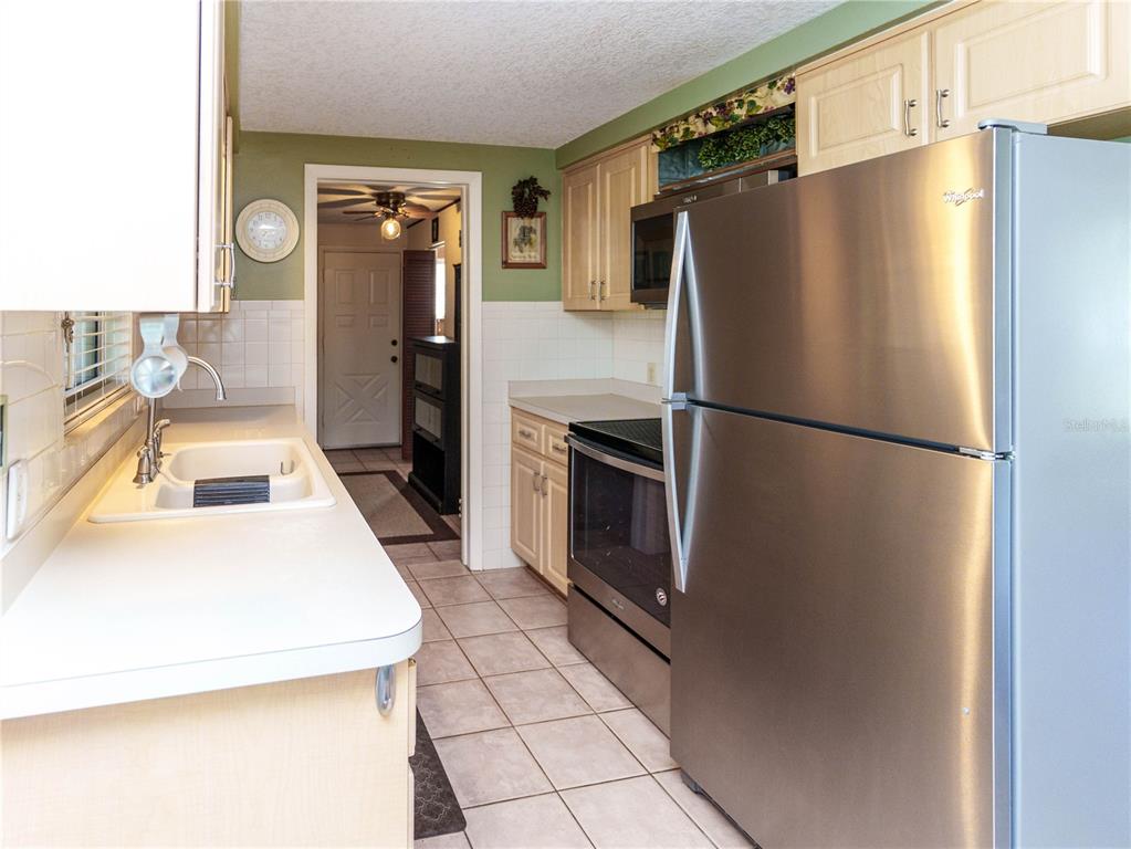 A kitchen features light wood cabinets, stainless steel appliances, white countertops, and tiled flooring — 6155 ILLINOIS AVENUE, NEW PORT RICHEY, FL