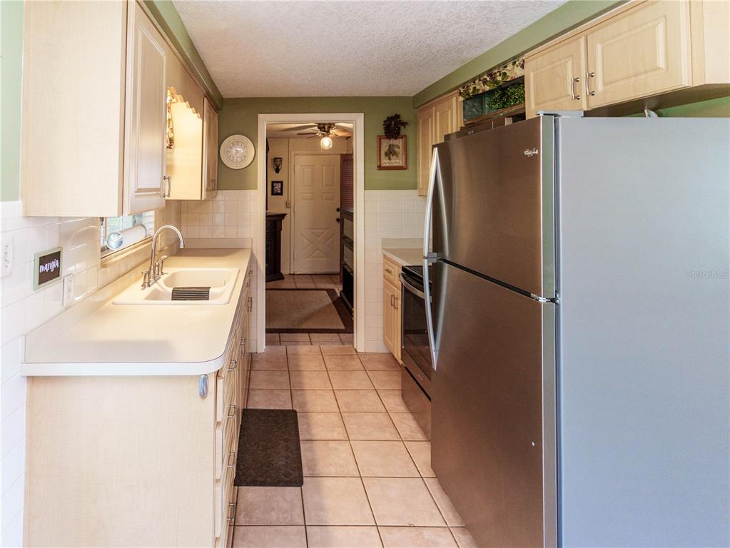 A galley kitchen features light wood cabinets, white countertops, stainless steel appliances, and tile flooring — 6155 ILLINOIS AVENUE, NEW PORT RICHEY, FL